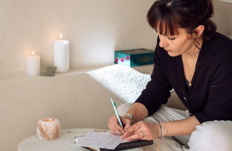 Femme écrivant dans un carnet, entourée de bougies et d'une lumière douce.