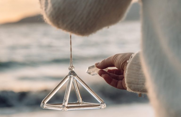 Une main tient un mobile en forme de pyramide au bord de la mer.
