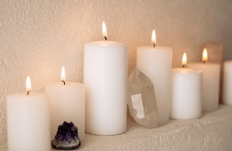 Six bougies blanches allumées sur une surface, accompagnées de cristaux.