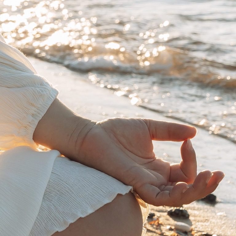 Main droite en position de méditation, paume levée, bord de la mer au coucher du soleil.