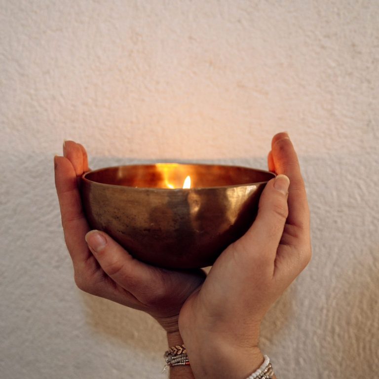 Des mains tenant un bol en métal, avec une flamme illuminant son intérieur.